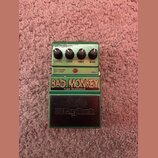 Zelený kytarový efekt s nápisy BAD MONKEY a TUBE OVERDRIVE. Na horní části jsou čtyři černé otočné ovířky s popiskem LEVEL, LOW, HIGH a GAIN. V horní…