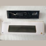 Fotografie zobrazuje černý Eurorack case s vloženým napájecím zdrojem a kabely, vedle jeho původního kartónového obalu. Na krabici je nápis EURORACK…