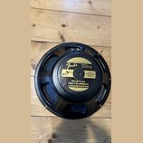 Černý reproduktor s kovovým rámem, položený na dřevěném povrchu. Na zadní straně je žlutá nálepka s nápisy „SPECIALLY DESIGNED FOR Fender MUSICAL INS…