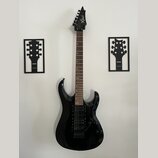 Černá elektrická kytara s hrotovitou hlavou a tmavým hnedým hmatníkem. Na hlavě je bílý nápis Xcart. Kytara má dva humbuckery, tremolo systém a je um…