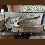 Elektrická kytara s tmavým, třpytivým povrchem v černém tvrdém kufru. Na hlavě kytary je viditelné logo ESP. Nástroj má dva humbuckery, jeden tónový…