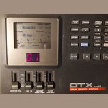 Černý elektronický modul s displejem a ovládacími prvky. Na spodní části je bílý nápis DTX Version 2.0 a pod ním červený pruh s textem DRUM TRIGGER M…