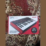 Fotografie zobrazuje krabici od MIDI kontroléru AKAI MPK mini. Na balení je zobrazen červený nástroj s klávesami a padem, doprovázený nápisy AKAI PRO…