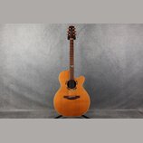 Akustická kytara s vyřezem (cutaway) v přirozené dřevěné barvě. Na hlavě je viditelné logo "Taylor". Hриф má v 12. poličce malý modrý ozdobný prvek.…