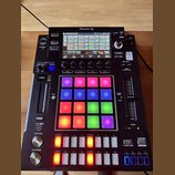 Černý sampler Pioneer DJ DJS-1000 s podsvícenými padovými políčky v různých barvách. Na horní straně je umístěn displej s ovládacími prvky a nápisy,…