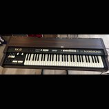 Hnědý elektronický orgán s klaviatura v dřevěném provedení. Na ovládacím panelu jsou nápisy XK-2 a HAMMOND. Jsou zde vidět bílé klávesy, tahové přepí…