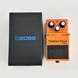 Oranžový kytarový efekt s černým spodním panelem a nápisy Distortion DS-1 a BOSS. Na horní části jsou tři černé otočné ovnovátka s popisky TONE, LEVE…