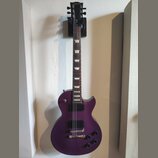 Fialová elektrická kytara s tvarem Les Paul, umístěná v nástěnním držáku. Na hlavě hředu je zlatý nápis Gibson. Kytara má dva humbuckery, čtyři ovlád…