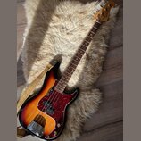 Elektrická basová kytara s tělem v barevné gradaci od žluté po černou (sunburst) a červeným vzorovaným pickguardem. Na hlavě hředu je viditelné logo…