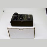 Černý kytarový efekt umístěný na bílém kartónovém krabici. Na horní straně jsou tři černé otočné knoflíky a nápisy Proton, envelope filter a Leaf Aud…