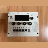 Bílý elektronický modul s nápisem Shruthi a logem Mutable Instruments. Zařízení má čtyři černé otočné ovladače označené čísly 1 až 4, pět malých zele…