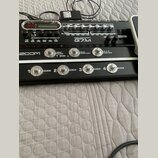 Černý kytarový procesor s nápisem GUITAR EFFECTS CONSOLE G2.1ut a logem ZOOM. Zařízení má digitální displej, několik ovládacích knoflíků a čtyři stou…