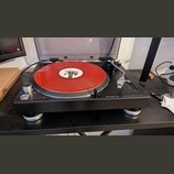 Černý turntable Pioneer DJ s nápisem DIRECT DRIVE TURNTABLE PLX-500. Na talíři je umístěna červená vinylová deska s bílým štítkem. Přístroj je vybave…