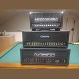 Tři kytarové zesilovače naskládané na sebe. Horní je černý s nápisem MEZZABARBA CUSTOM AMPLIFICATION, prostřední má logo CERIATONE AMPLIFICATION a ná…