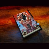 Kytarový efekt s kovovým šasi a dřevěným panelem v přední části. Na panelu jsou nápisy Taurus BASS Servo, Custom Edition a označení ovládacích prvků…