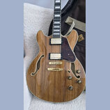 Polodupatá elektrická kytara s přírodním dřevěným povrchem a f-otvory. Nástroj má dva humbuckery, zlatý most a zlaté ovládací knoflíky. Na kytaru je…