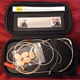 Černý přepravní pouzdro s mikrofonem a příslušením. Uvnitř je béžový headset s červeným konektorem a plastový sáček s několika pěnovými větříky. V ho…