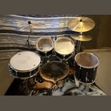 Sada bubnů v černé barvě s kovovými obručemi a dvěma cymbály. Na horním cymbálu je viditelné logo Pearl. Povrchy blan bubnů vykazují známky opotřeben…