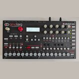 Černý analogový syntetizátor značky Elektron s nápisem „analog FOUR 4 Voice Analog Synthesizer“. Přístroj má v horní části displej, několik otočných…