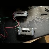 Dvě elektrické kytarové snímače typu humbucker s černým plastovým krytem a viditelnými póly. Na spodní straně jednoho ze snímačů je bílá nálepka s ná…