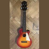 Akustická kytara s tělem v červeno-žlutém sunburst provedení a černou hlavou. Na hlavě je bílý nápis Epiphone a podpis Lee Perry. Nástroj má hnědý hm…