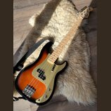 Elektrická basová kytara s tělem v provedení sunburst a zlatým pickguardem. Na hlavě hředu je viditelné logo Squier. Nástroj má světlou dřevěnou hmat…