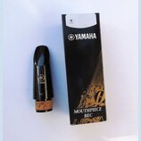 Černý munzpun s korkem v dolní části a přiloženým černým papírovým krabicí. Na munzpunu i na krabici je bílé logo a nápis YAMAHA, na munzpunu je dále…