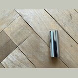 Na dřevěné podlaze leží krátký, válcový předmět z lesklého, chromovaného kovu. Povrch je hladký a zrcadlový, bez viditelných nápisů, značek či poškoz…