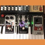 Tři kytarové efekty značky electro-harmonix umístěné vedle sebe na klávesovém nástroji. Zleva je bílý pedál s nápisem PITCH FORK, prostřední je černý…