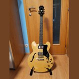 Světle žlutá polodublová elektrická kytara s černým hmatníkem a černým pickguardem. Na hlavě je bílý nápis Epiphone. Kytara má dva humbuckery, čtyři…