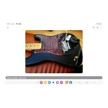 Černá elektrická kytara s červeným mramorovaným pickguardem a světlým hnedým hmatníkem. Nástroj má tři snímače typu single-coil, třetí knoflík a pěti…