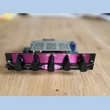 Černý kytarový zesilovač s fialovým předním panelem. Na panelu jsou čtyři černé otočné knofíky s nápisy DRIVE, BASS, MIDDLE PULL/CHANNEL a TREBLE, dá…