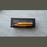Zlatý kovový mouthpiece na saxofon položený na černé krabičce. Na krabičce je bílý nápis NADIRSAXWIND.COM a na mouthpieceu je vyryté logo TD. Povrch…