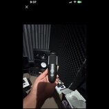 Černý dynamický mikrofon s mřížkou v horní části. Na těle je viditelné logo AKG a pod ním nečitelný nápis modelu. Mikrofon drží ruka, v pozadí jsou v…