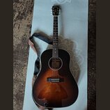 Akustická kytara s tělem v provedení sunburst (přechod od černé k hnědé). Na hlavě je bílý nápis Cort. Kytara má černý popruh s barevným vzorem na ok…