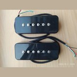 Dvě černé kytarové humbuckery s kovovými ladicími šrouby. Nástroje jsou provedeny v černé barvě s lesklým povrchem, na kterém jsou viditelné drobné š…