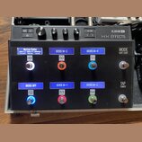 Černý kytarový efektový pedalboard s nápisem LINE 6 HX EFFECTS. Horní část obsahuje ovládací knoflíky a tlačítka SAVE, ACTION a HOME. Spodní část obs…