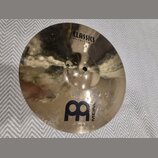 Zlatý kovový činel s viditelným broušením povrchu. Na číneli jsou černé nápisy CLASSICS CUSTOM a MEINL spolu s logem ve tvaru dvou propojených písmen…