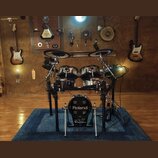 Elektronická bicí souprava značky Roland umístěná na modrém koberci. Na basovém bubnu je bílý nápis Roland a níže logo V-Drums. Souprava obsahuje dva…