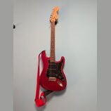 červená elektrická kytara s černým pickguardem a dřevěným hřidnicí. Na hlavě je viditelné logo Fender. Kytara má připojený červený popruh a visí na n…