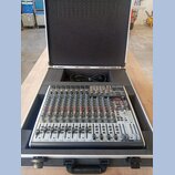 Míchací pult v ochranném přepravním kufru s černým polstrováním. Na horním pravém rohu je viditelné logo "Behringer". Zařízení obsahuje řadu faderů,…