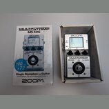 Fotografie zobrazuje stříbrný efektový pedál v krabici vedle původního obalu. Na zařízení i na krabici je vidět logo ZOOM a nápis MULTISTOMP MS-50G f…