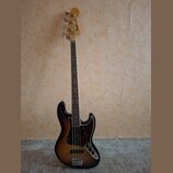 Elektrická basová kytara s tělem v provedení sunburst a hnědým hmatníkem. Na hlavě je viditelné logo Fender a nápis Jazz Bass. Kytara má tmavý pickgu…