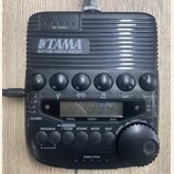 Černý rytmický doprovod TAMA RHYTHM WATCH RW200 s digitálním displejem a ovládacími tlačítky. Na horní části je nápis TAP TEMPO a vprostřed logo TAMA…