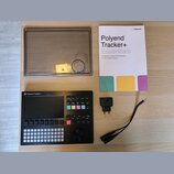 Na fotografii je černý sekvencer Polyend Tracker + s displejem a řadou tlačítek. Součástí sady je průhledný plastový kryt, napájecí adaptér a printed…