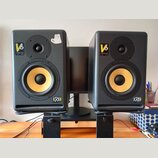 Pár černých studiových monitorů s žlutými membránami basových reproduktorů. Na obou je vidět nápis V6 a logo KRK SYSTEMS. Levý reproduktor má v horní…