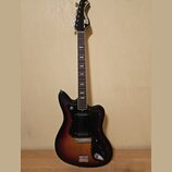 Elektrická kytara s trupem v tmavém sunburst provedení a černým pickguardem. Na hlavě hředu je bílý nápis „Musima der Luther“. Nástroj vykazuje známk…
