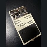 Bílý efekt pedál s černým nášlapným spínáčem a nápisem BOSS. Na horní straně jsou čtyři černé otočné ovratidla a nápisy CHECK, THRESHOLD, DECAY, REDU…