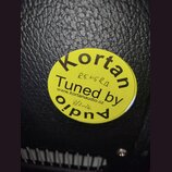 Kruhová žlutá nálepka s černým textem nalepená na černém povrchu z imitace kůže. Na nálepce je nápis Kortan Tuned by Audio a webová adresa www.kortan…