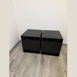Dvě černé, kostkovité basové reproduktory s matným povrchem. Na přední straně každého boxu je vyryt nápis L-o. V horní a spodní části jsou viditelné…